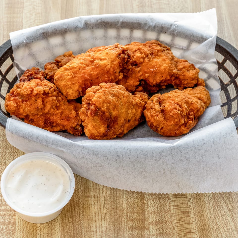 A basket of crispy fried chicken pieces with a side of ranch dressing on a wooden table.