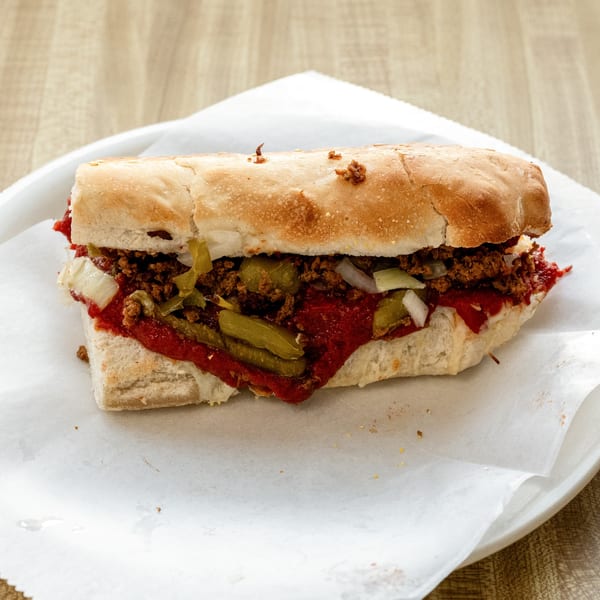 A Raydee Magoo's pizza sub with meat, sauce, pickles, and onions on a white plate.
