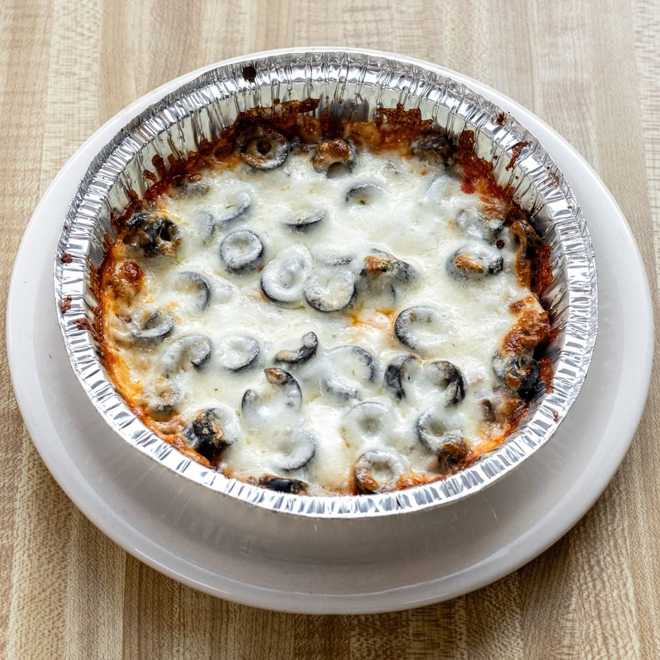 Baked pizza dip with melted cheese and black olives in a foil pan on a white plate.