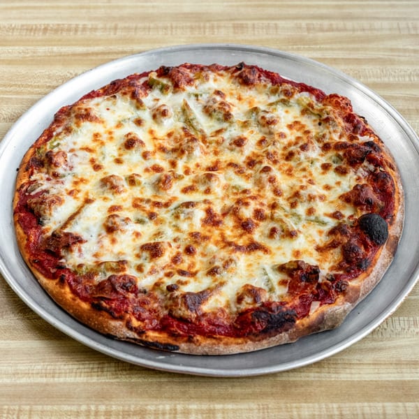 A whole Raydee Magoo's pizza with melted cheese, sausage, and green peppers on a metal pan.